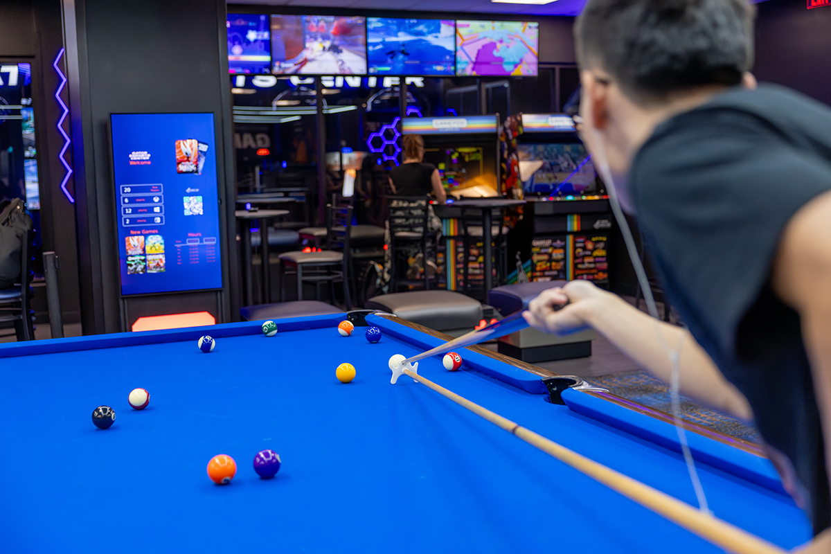 A student uses a pool cue bridge to line up a shot at a billiards table inside the Reitz Union Game Room.
