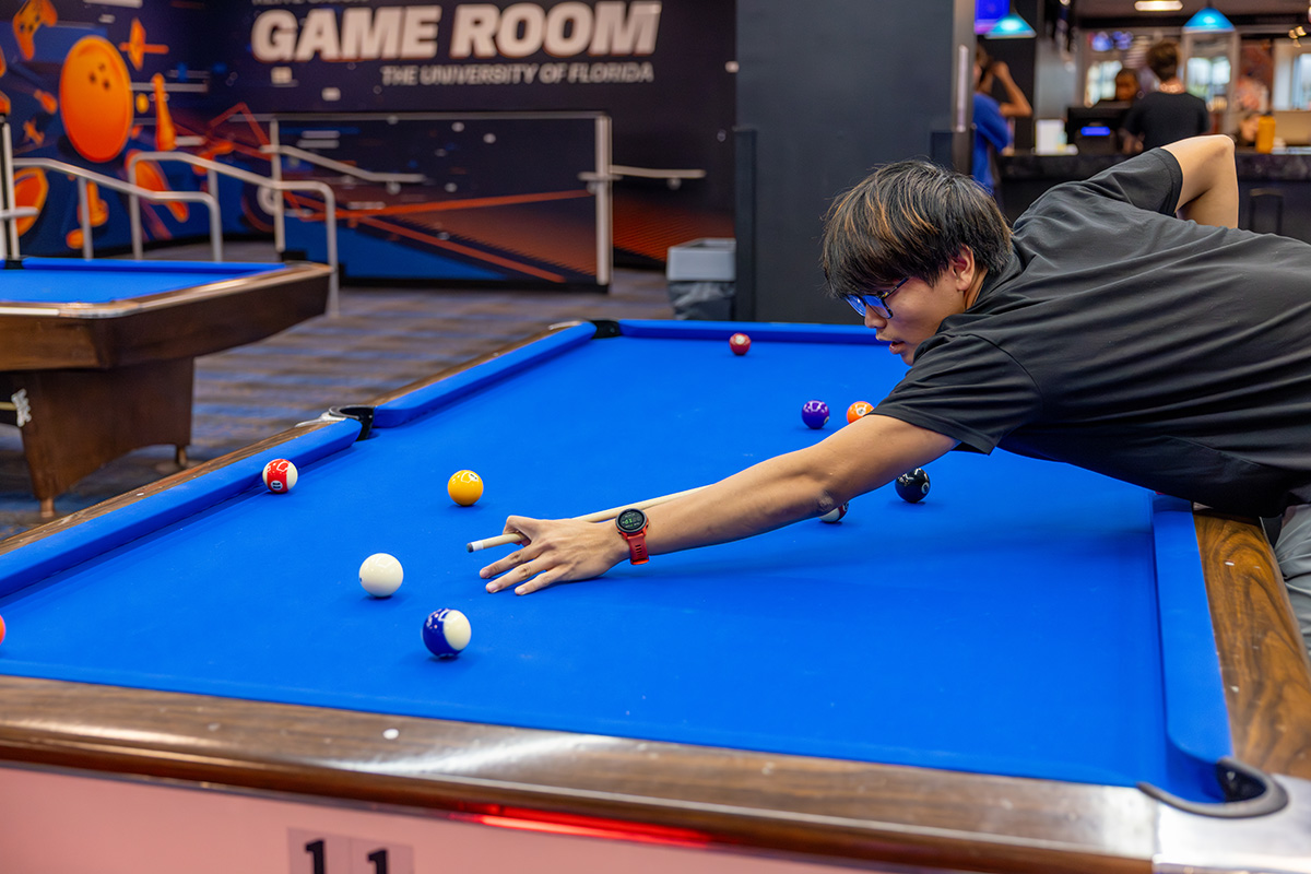 Student leans over a billards table to line up a pool shot inside the Reitz Union Game Room.