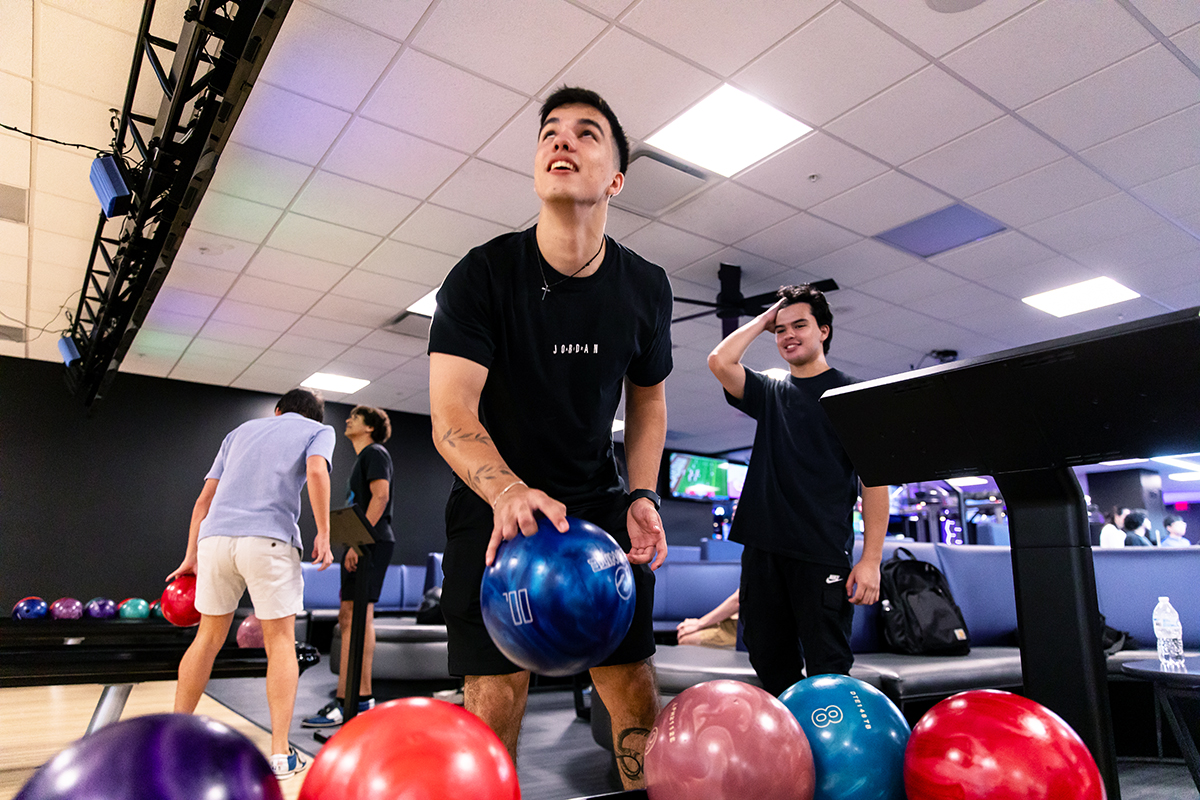 A person grabbing a bowling ball from the ball return and looks up to view their current score from the display overhead.